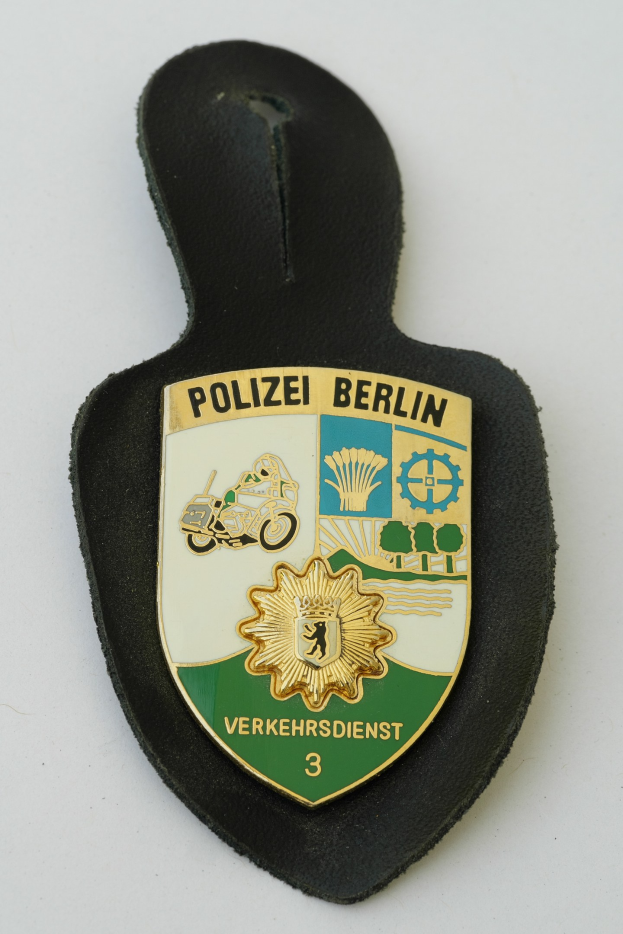 Ein schildförmiges Polizeibadge von Berlin mit einem blauen Hintergrund, weißer Umrandung und einem zentralen weißen Stern, auf dem 'Polizei Berlin' in schwarzer fetter Schrift steht.