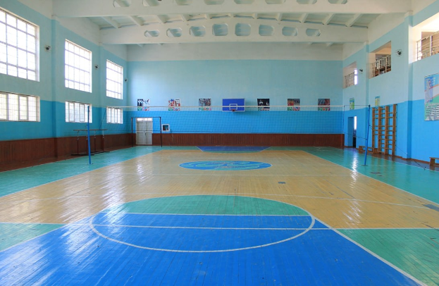 Großer Turnhallen mit blau-weißem Boden, Basketballfeld, Netz, Stangen, Tür, Fenstern, Wandplakaten, Geländer und Dach.