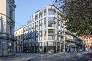 Großes Bürogebäude mit vielen Fenstern, umgeben von Straßeninfrastruktur, Fahrzeugen, Fußgängern, Bäumen und einem bewölkten Himmel, das als neue Firmenzentrale dient.