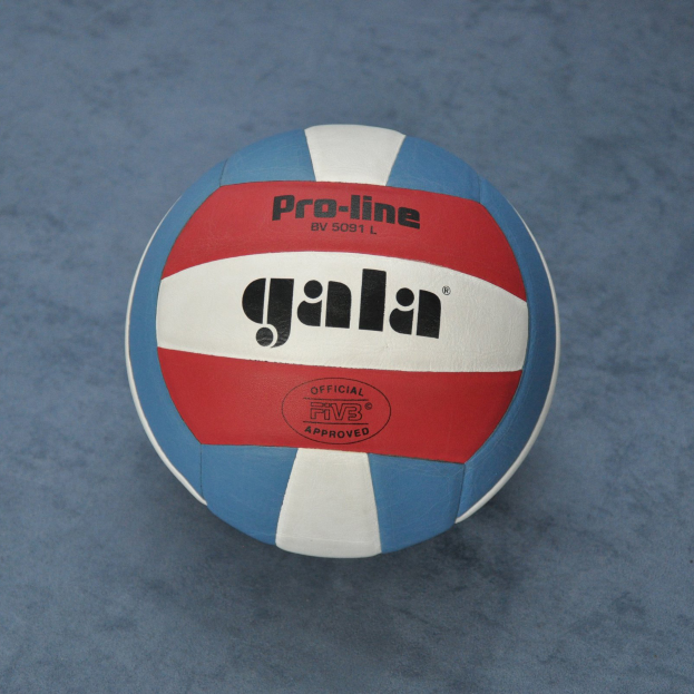 Ein blauer und roter Volleyball mit dem Wort "Gala" darauf, der auf einer blauen Fläche steht.