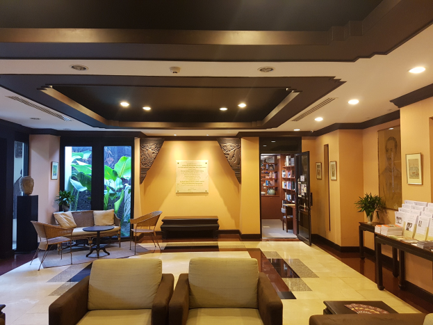 Ein geräumiger Hotelfoyer mit Sitzbereichen, Dekorationspflanzen, Bücherregalen, Leuchten, Wandbildern und Beistelltisch-Dekoration, beleuchtet von natürlichem Licht durch Fenster und Türen.