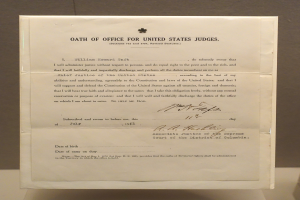 Ein Blatt mit dem Text "Dienstpflicht für United States Richter" darauf, das vor einer Wand auf einem Tisch liegt.