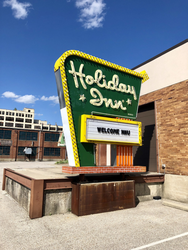 Holiday Inn Schilder an der Seite eines Gebäudes mit einem Textboard vorne auf dem Boden, bewölkter Himmel darüber.