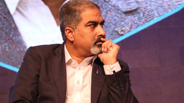 Ein Mann im Anzug auf einer Bühne, der tief nachdenklich vor einem Bildschirm sitzt.