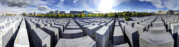 Luftaufnahme des Holocaust-Mahnmals für die ermordeten Juden Europas in Berlin, Deutschland, mit großen Betonplatten, umgeben von Bäumen, Gebäuden und Fahrzeugen auf einer Straße mit einem bewölkten Himmel.