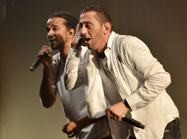 Zwei Männer in legerer Kleidung treten auf der Bühne auf, jeder hält ein Mikrofon in der Hand.