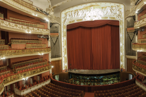 Großer Innenraum mit roter Gardine, Sitzplätzen, Geländern, Beleuchtung, Wandskulpturen und Bühnenobjekten, der an einen Konzertsaal erinnert.