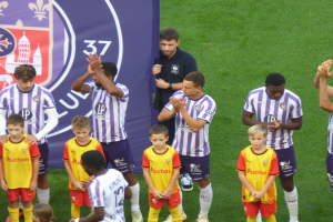 Eine Gruppe junger Jungs auf einem Fußballfeld, die klatschen, mit einem Banner mit Text und Logos im Hintergrund.