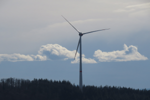 Windkraftanlage im Wald mit bewölktem Himmel und Hügel im Hintergrund.