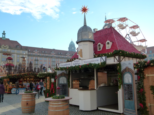 Ein geschäftiges Weihnachtsmarkt in Nürnberg, Deutschland, mit Menschen um geschmückte Stände, festliche Lichter, ein Riesenrad, Gebäude und einen bewölkten Himmel, mit einer Tafel mit Text auf der rechten Seite.
