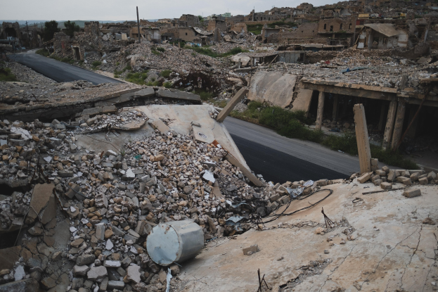 Zerstörtes Gebäude in Aleppo mit Schutt und Trümmern auf der Straße verstreut, Straße im Vordergrund, Himmel im Hintergrund.