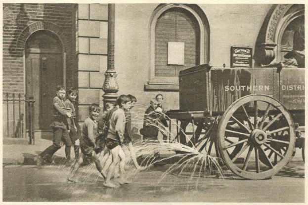 Feuerwehrleute in Schutzausrüstung mit einem, der einen Schlauch hält, einem Pfahl im Hintergrund, einem bewölkten Himmel und Rohren auf der rechten Seite.