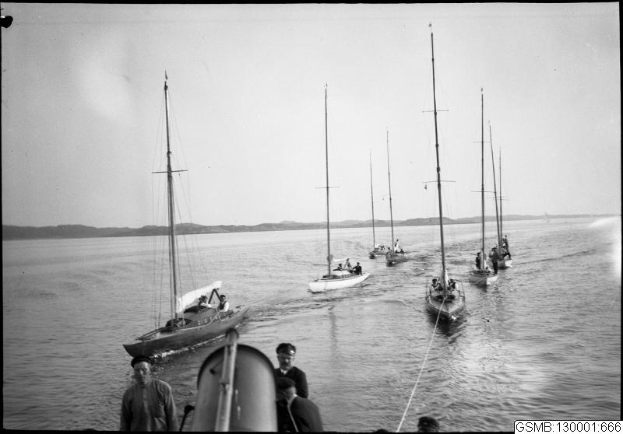 Ein Schwarz-Weiß-Foto von mehreren Segelbooten bei einem Rennen im Wasser mit Menschen an Bord, mit Hügeln und einem klaren Himmel im Hintergrund und einem Text unten, der "Segelbootrennen in San Francisco, Kalifornien" lautet.
