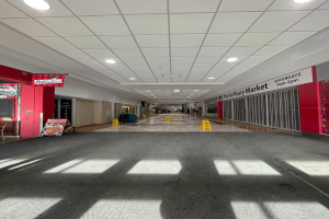 Innenseite eines Einkaufszentrums mit Deckenbeleuchtung, einem Stuhl und einer Tafel, die links " Sydbury Market - Vorher und Nachher " lautet, und verstreuten Gegenständen auf der rechten und Boden.