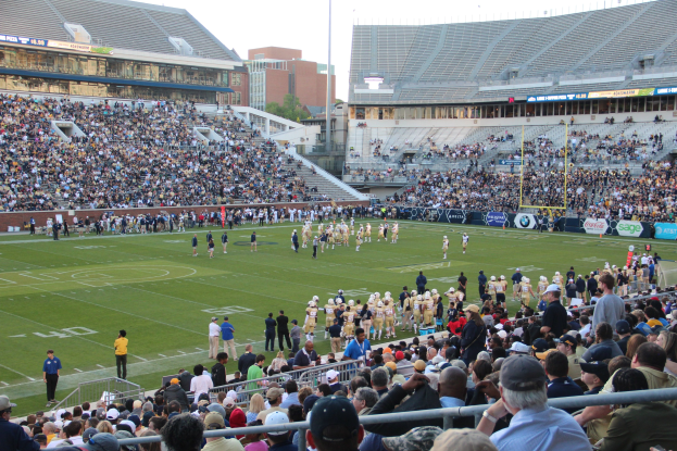 Fußballspiel in einem Stadion mit Spielern auf dem Feld und Zuschauern in den Rängen.
