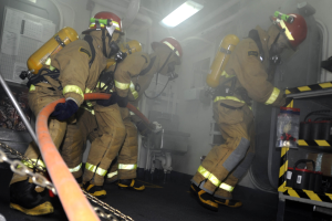 Feuerwehrleute in Schutzausrüstung arbeiten an einem Feuerlöschfahrzeug mit Ausrüstungsgestellen und Hintergrundinfrastruktur.
