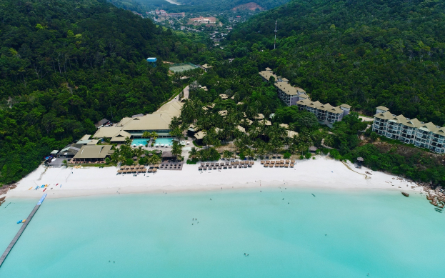 Luftaufnahme eines Strandresorts in Koh Samui, Thailand, mit einer Brücke auf der linken Seite, Gebäuden, Bäumen, Hügeln und Menschen am Strand.