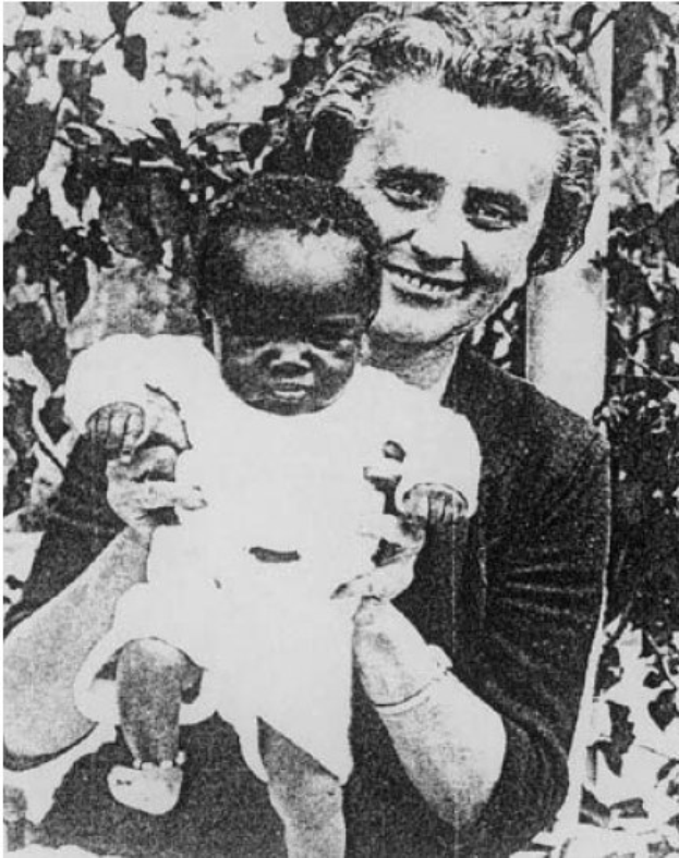 Ein Schwarz-Weiß-Foto einer Frau, die lächelt, während sie ein Baby hält, mit Blättern im Hintergrund.