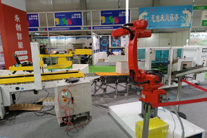 Gruppe von Robotern auf einem Tisch in einer Fabrikumgebung mit Maschinen, Kabeln, Texttafeln, Lampen und Menschen im Hintergrund.