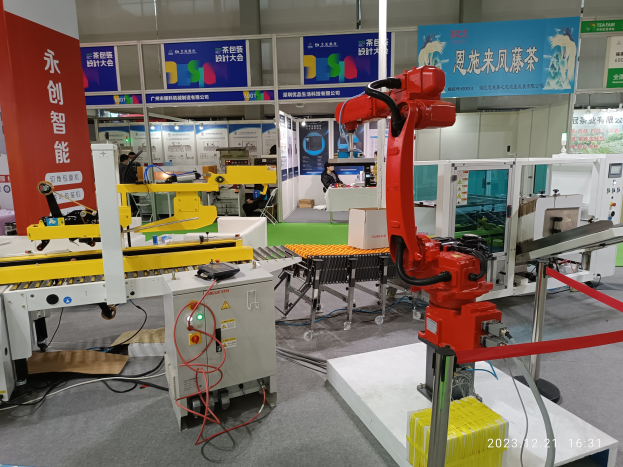 Gruppe von Robotern auf einem Tisch in einer Fabrikumgebung mit Maschinen, Kabeln, Texttafeln, Lampen und Menschen im Hintergrund.