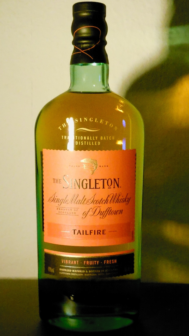 Eine tiefe bernsteinfarbene Flasche Singleton of Dufftown Tailfire Single Malt Scotch Whisky mit einem schwarzen Etikett, das eine Löwen- und Burg-Kresta zeigt.