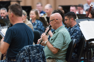 Eine Gruppe von Männern, die Klarinetten in einem Raum mit Bücher auf Ständern vor ihnen spielen.
