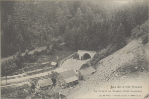 Altes Schwarz-Weiß-Foto einer kleinen Stadt mit Häusern, einer Brücke und Bäumen im Hintergrund, mit Text unten.
