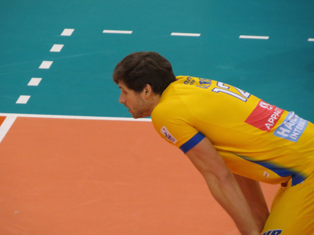 Eine professionelle Volleyballspielerin in einem gelben T-Shirt mit der Aufschrift "Volleyball" steht selbstbewusst auf einem Court und bereitet sich auf den Aufschlag vor.