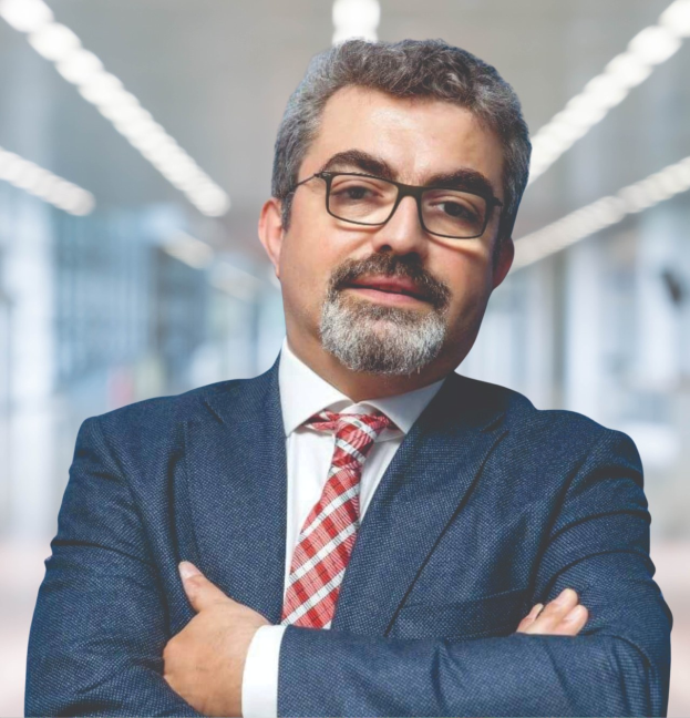 Ein Mann in Anzug und Krawatte mit verschränkten Armen und Brille, der vor einem unscharfen Hintergrund steht, als neuer Marketingchef bezeichnet.