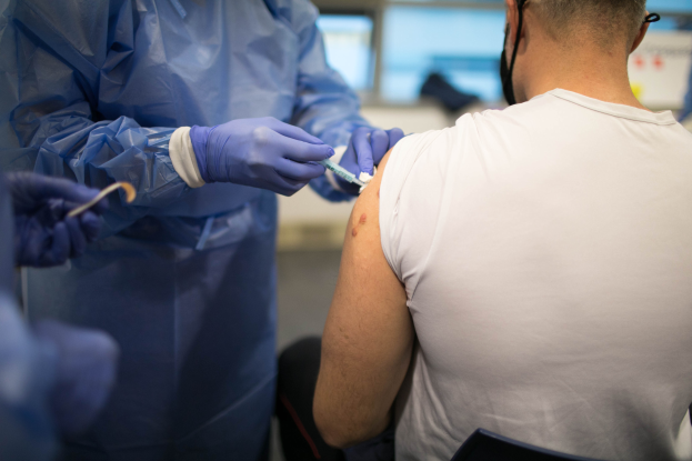 Ein Mann in einem weißen Hemd erhält eine Impfung von einem Arzt in einer blauen Kleidung und Handschuhen, der eine Spritze hält, mit einem unscharfen Hintergrund.