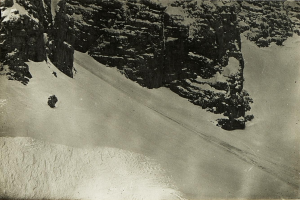 Ein Schwarz-Weiß-Foto eines Menschen, der eine schneebedeckte Bergabhänge hinabskit, umgeben von schneebedeckten Hängen, mit Text am unteren Rand.