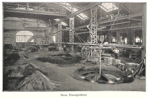 Ein altes Schwarz-Weiß-Foto einer Fabrik mit Arbeitern, die eine Maschine bedienen, umgeben von Metallstangen und -pfosten, mit Text unten: "Neue Eisenglebeerei, die erste Fabrik Deutschlands."