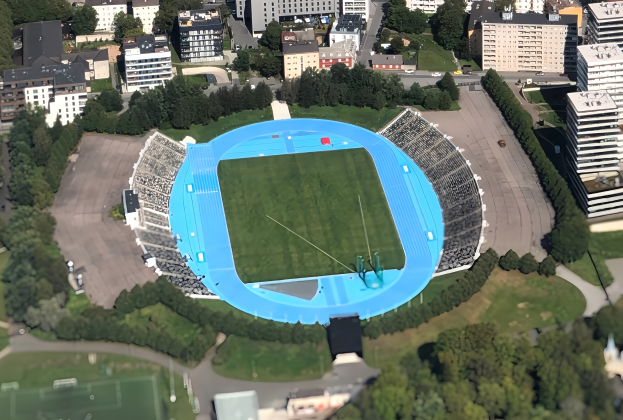 Luftaufnahme des Münchner Olympiastadions umgeben von Stadtgebäuden, Bäumen, Straßen, Fahrzeugen und Gras.