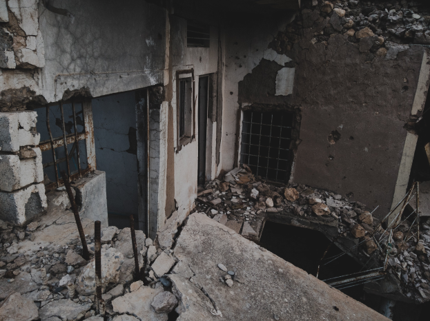 Ein altes, bröckelndes Gebäude mit zerbrochenen Fenstern und herumliegendem Schutt, das auf einen Zustand des Verfalls und der Vernachlässigung hinweist.