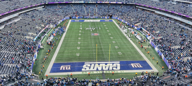 Ein voller Fußballstadion mit Spielern auf dem Feld, Zuschauern auf den Sitzen und Texttafeln rundherum.