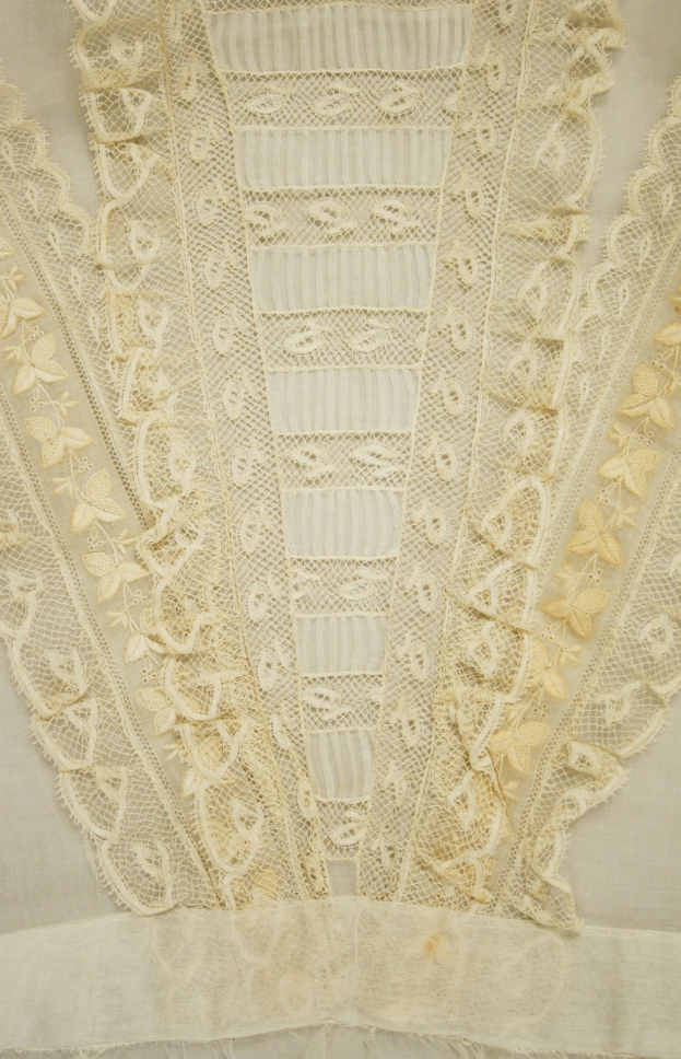 Nahaufnahme eines weißen Kleides mit zarter, detailreicher Spitzenverzierung, die verschiedene Muster und Formen aufweist und aus leichtem, luftigem Stoff besteht, der für den Sommer geeignet ist.