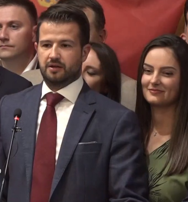 Ein Mann im Anzug spricht in ein Mikrofon auf einem Podium, mit einem Banner dahinter, zu einer Menge über ein vom Staat verhängtes Verbot von Social Media.