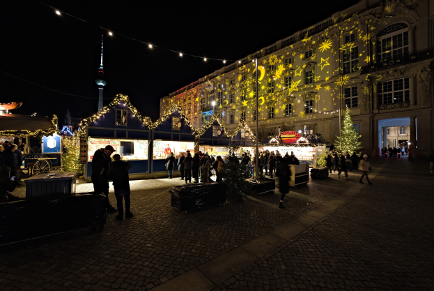 Ein belebter Weihnachtsmarkt in Berlin, Deutschland mit Menschen um dekorierte Stände, festliche Lichter und dunklen Himmel im Hintergrund.