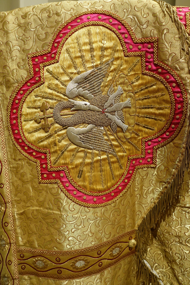 Nahaufnahme eines Priestergewandes mit goldenen und roten Stickereien und detaillierten Verzierungen vor einem Wandhintergrund.