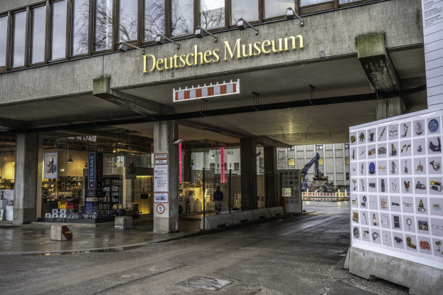 Außenansicht des Deutschen Museums in Berlin: großes Gebäude mit Glasfenstern, Säulen und Namensschild, daneben Informationsschild, Bäume, andere Gebäude und Himmel im Hintergrund.