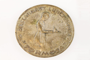 Eine goldene Medaille mit einer Frau, die ein Tablett mit Essen hält, mit Text und einem Personenbild, vor einem weißen Hintergrund.