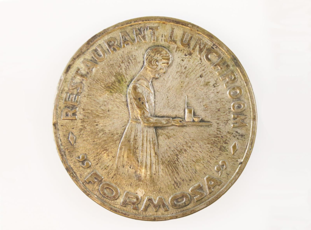 Eine goldene Medaille mit einer Frau, die ein Tablett mit Essen hält, mit Text und einem Personenbild, vor einem weißen Hintergrund.