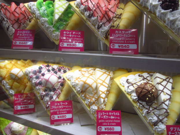 Vitrine mit verschiedenen Sorten Eis, jede mit einem Preisschild, in unterschiedlichen Farben, Formen und Geschmacksrichtungen angeordnet.