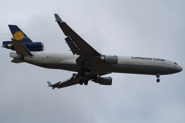 Ein Lufthansa Cargo Boeing 777-300ER im Flug, mit ausgefahrenen Flügeln und aktivierten Triebwerken, mit sichtbarem Text auf dem Rumpf gegen einen wolkengefüllten Himmel.