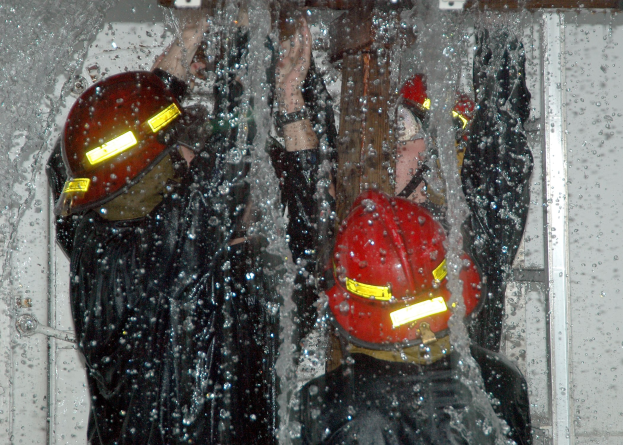 Drei Feuerwehrleute in schwarzen Uniformen und roten Helmen stehen in einem wassergeschädigten Raum und arbeiten zusammen, um ein Feuer zu löschen.