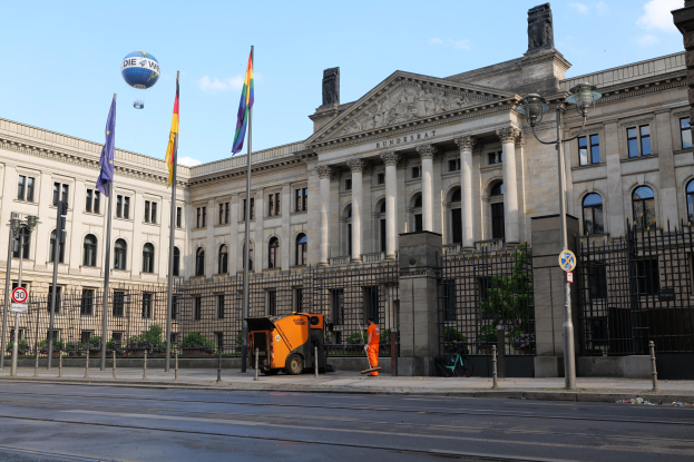 Großes modernes Gebäude mit zahlreichen Fenstern, als Bundestag in Berlin, Deutschland identifiziert, umgeben von Straßeninfrastruktur, Fahrzeugen, Passanten und Bäumen unter einem bewölktem Himmel.