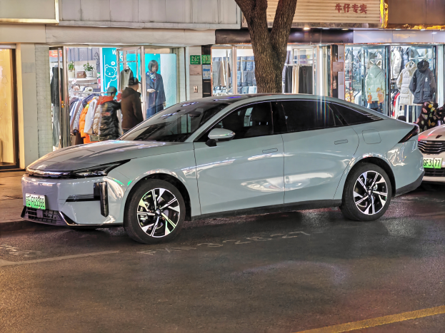Ein Mitsubishi Lancer EV Elektroauto auf der Straße bei Nacht, umgeben von Gebäuden, Geschäften, Schaufensterpuppen, Schildern und Lichtern.