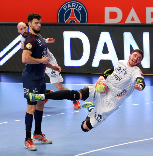 Eine Gruppe von Männern, die Handball auf einem Platz spielen, einer hält einen Ball, mit einem Hintergrundschild der Paris Saint-Germain Futsal-Mannschaft.