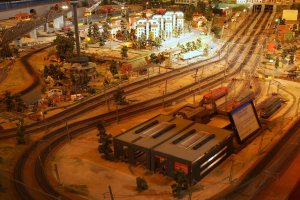 Eine detaillierte Modellbahnausstellung in einem Museum, mit einer Miniaturstadtlandschaft mit Gebäuden, Bäumen, Schienen, Fahrzeugen, Polen, Lichtern und Schildern.