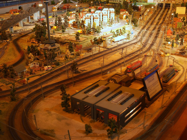 Eine detaillierte Modellbahnausstellung in einem Museum, mit einer Miniaturstadtlandschaft mit Gebäuden, Bäumen, Schienen, Fahrzeugen, Polen, Lichtern und Schildern.